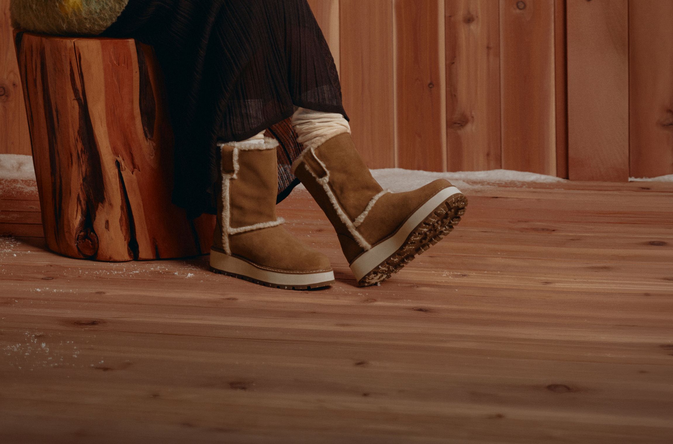 Tan Merrell winter boots beside a wooden cabin wall.